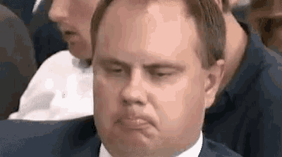 a man is making a funny face while sitting in a crowd of people .