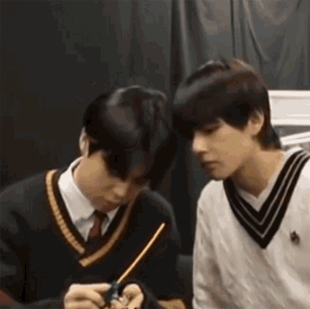 two young men are sitting next to each other and one of them is holding a pencil .