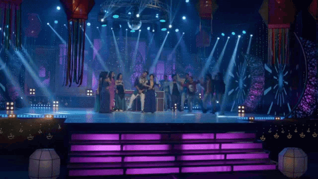a group of people are dancing on a stage in front of purple lights