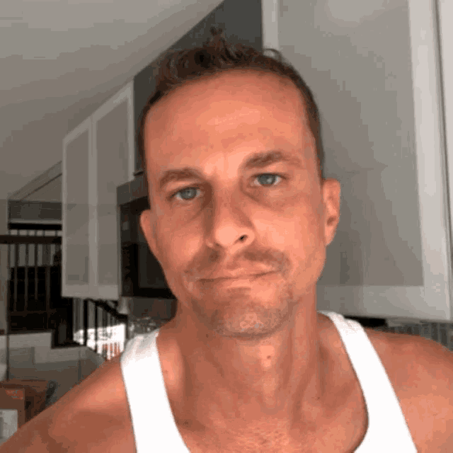 a man in a white tank top looks at the camera with a serious look on his face