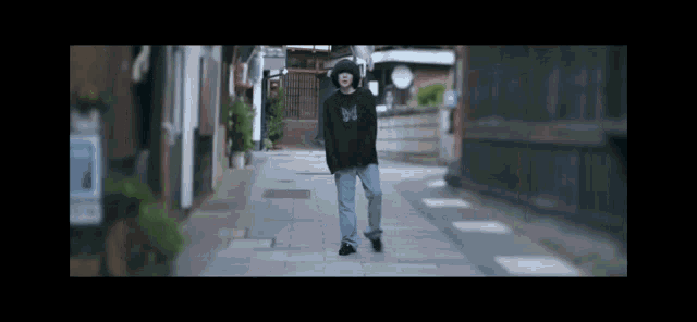 a person wearing a black sweatshirt with a butterfly on it is walking down a street .