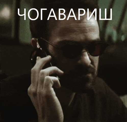 a man wearing sunglasses is talking on a cell phone under a sign that says " chogavarish "