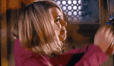 a woman in a pink shirt is looking at something in a dark room