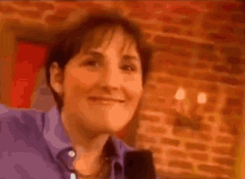 a woman in a purple shirt is making a face in front of a brick wall