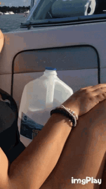 a gallon of water sits on someone 's lap in front of a boat with a watermark that says imgplay