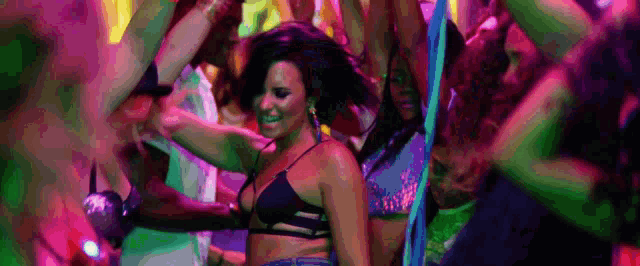 a woman in a black bikini top is dancing in a crowd of people at a party .
