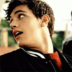 a young man with a surprised look on his face is wearing a black jacket and red sweater .