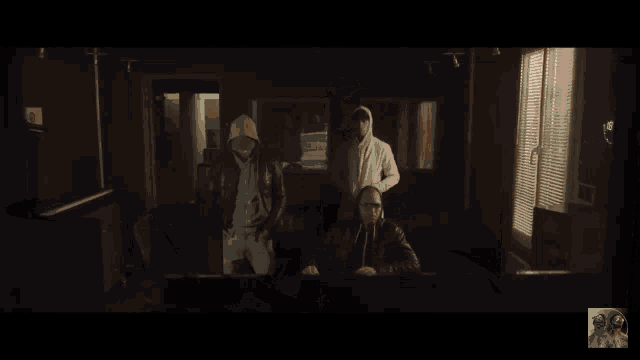 a group of men are standing in a dark room and one of them is wearing a white hoodie