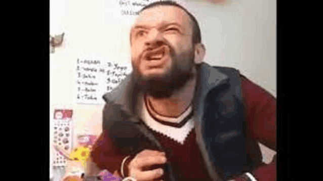 a man with a beard and a vest is making a funny face while sitting at a table .