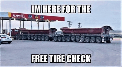a large dump truck is parked in front of a gas station with a sign that says im here for the free tire check .
