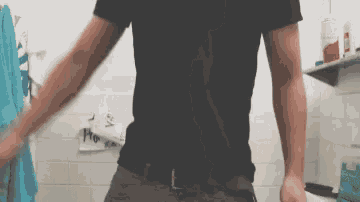 a man in a black shirt is standing in a bathroom with his arms outstretched ..