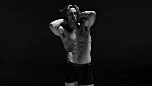 a shirtless man in calvin klein underwear is standing in a dark room .