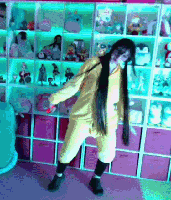 a woman in a yellow hoodie is dancing in front of a shelf full of stuffed animals