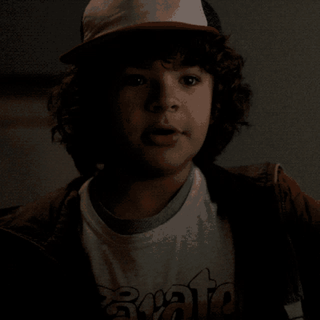 a boy with curly hair wearing a hat and a shirt that says roots