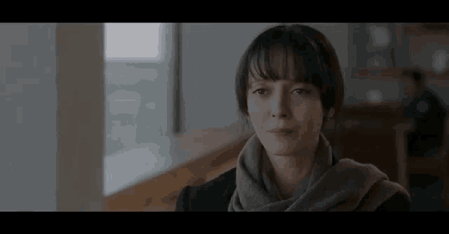a woman wearing a scarf is sitting in front of a window in a room .