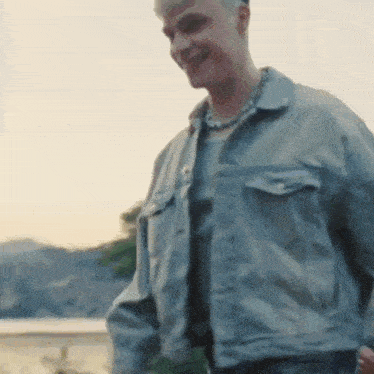 a man wearing a denim jacket and a necklace is standing in front of a building .