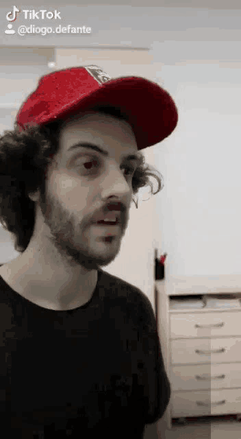 a man with a beard wearing a red hat and black shirt .
