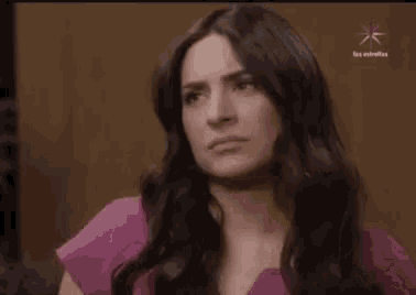 a woman with long black hair is wearing a pink shirt and making a face .