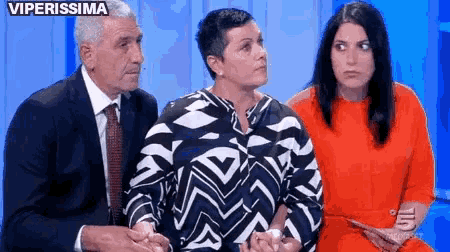 a man in a suit and tie is sitting next to two women and a woman in an orange dress .