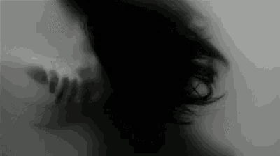 a black and white photo of a woman 's face with a hand behind her .