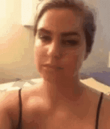 a woman in a black tank top is making a funny face while sitting on a bed .