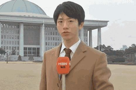 a young man wearing a suit and tie is holding a microphone in front of a building .