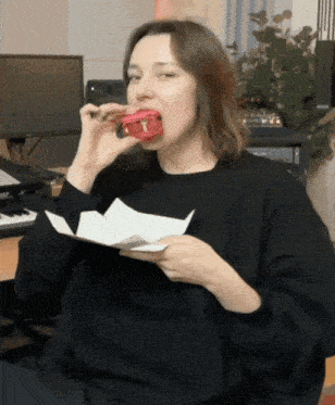 a woman in a black sweater is eating a hamburger