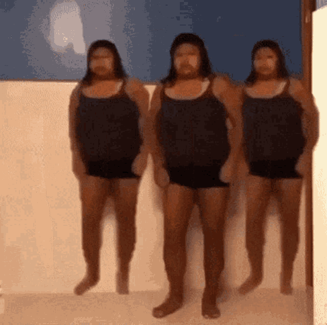 three people in black tank tops and shorts are standing in a room