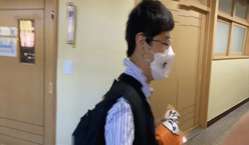 a man wearing a mask and a backpack walking down a hallway