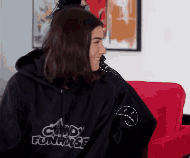 a woman wearing a black candy funhouse hoodie sits on a red chair