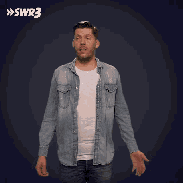 a man in a denim shirt is standing with his arms outstretched in front of a swr3 sign