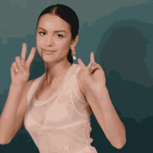 a woman in a white tank top is making a peace sign with her hands