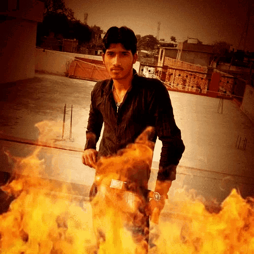 a man in a black shirt stands in front of a large fire
