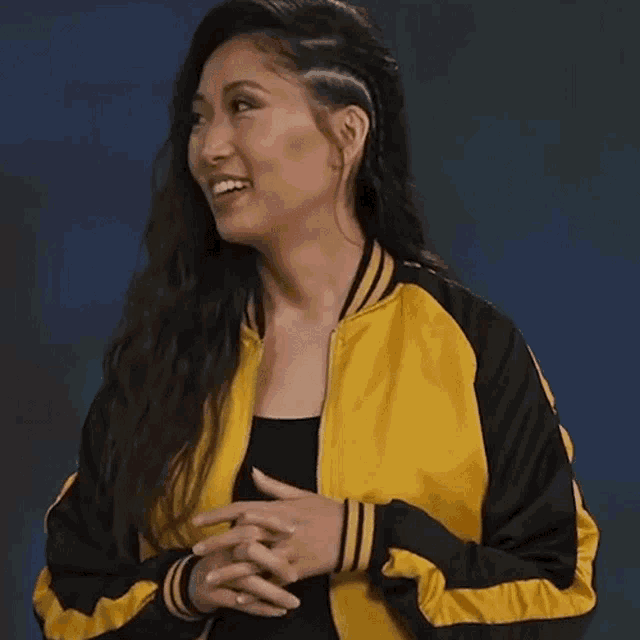 a woman wearing a yellow and black jacket is holding her hands together and says ohh !