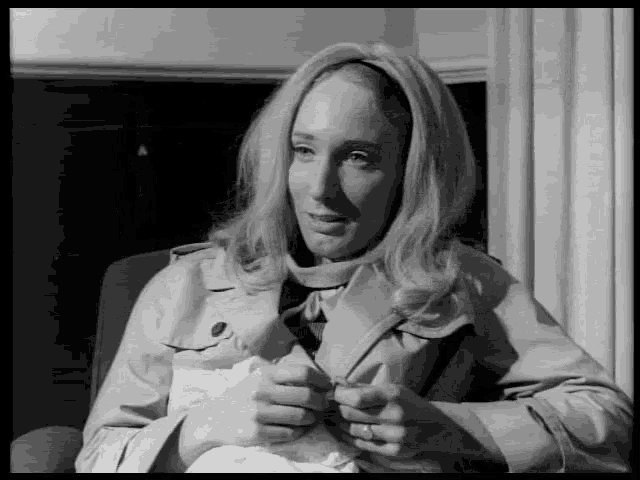 a woman in a trench coat is sitting in a chair holding a piece of paper