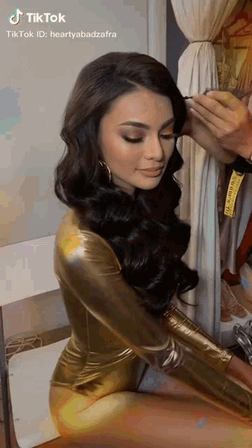 a woman in a gold bodysuit is getting her makeup applied