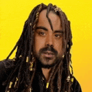 a man with dreadlocks and a beard is wearing a black shirt .