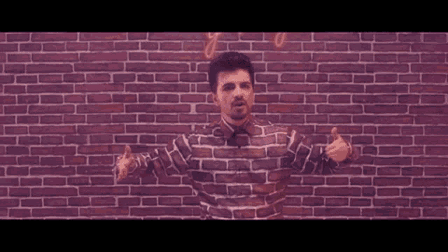 a man with a beard is standing in front of a brick wall and making a funny face .