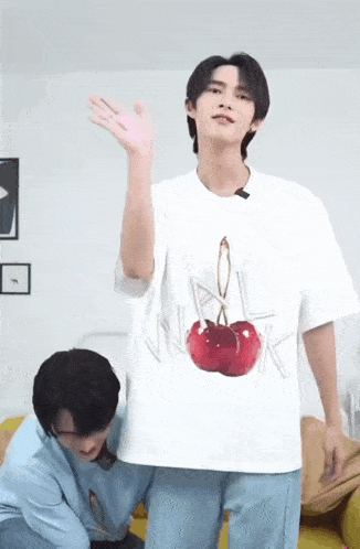 a man wearing a white t-shirt with two cherries on it is waving at the camera .