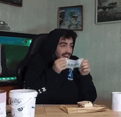 a man in a black hoodie is sitting at a table with a bucket and a piece of cake .