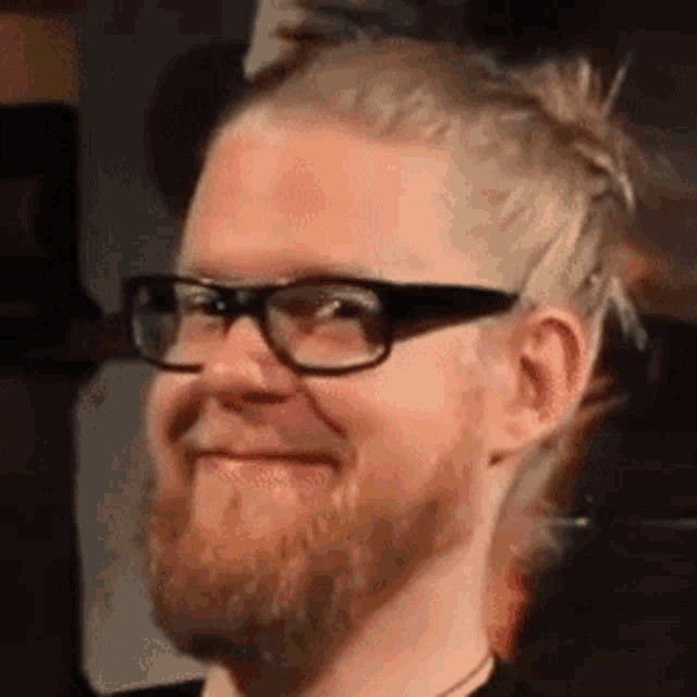 a man with a beard wearing glasses and a bun is smiling .