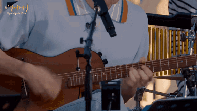 a man is playing a guitar in front of a microphone with a foreign language written on the bottom right