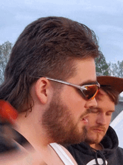 a man with a mullet and sunglasses looks to his left