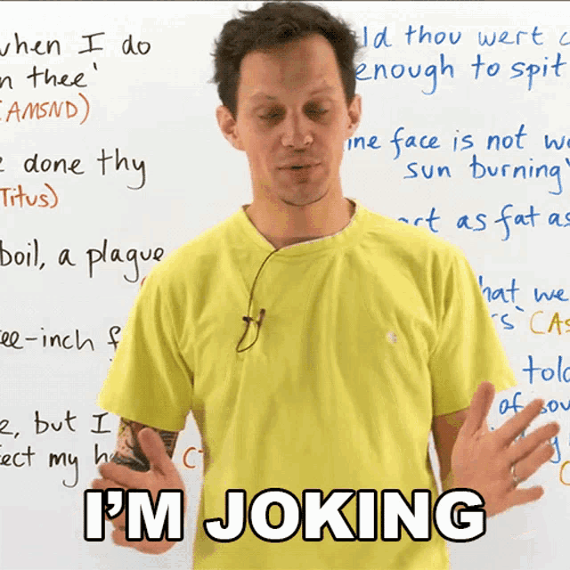 a man in a yellow shirt stands in front of a white board that says " i 'm joking "