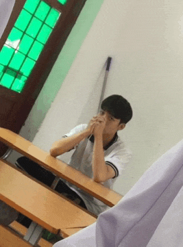 a young boy sits at a desk with his hands folded