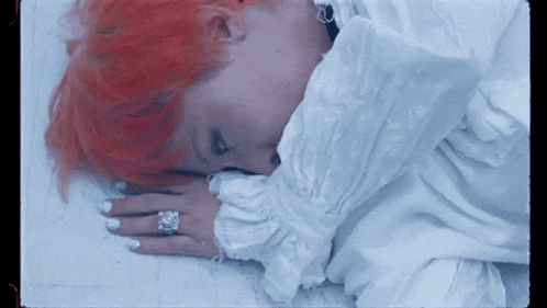 a woman with red hair is laying down with her head on her hand