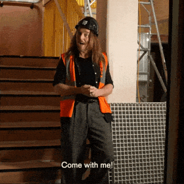 a man with long hair wearing a hard hat and an orange vest says come with me