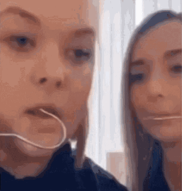 two young women are playing with a toothpick in their mouths .