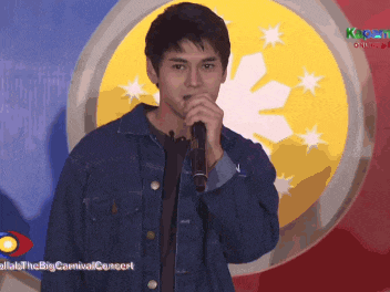 a man in a denim jacket sings into a microphone in front of a flag