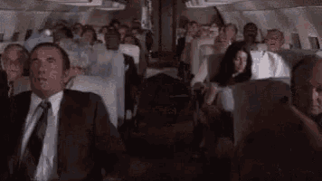 a man in a suit and tie is sitting on a plane with a crowd of people .
